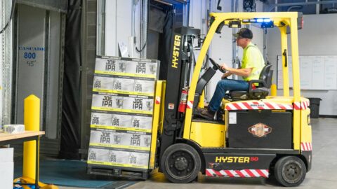 man riding a yellow forklift lifting boxes