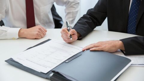 a person in black suit holding a pen near the documents on the table